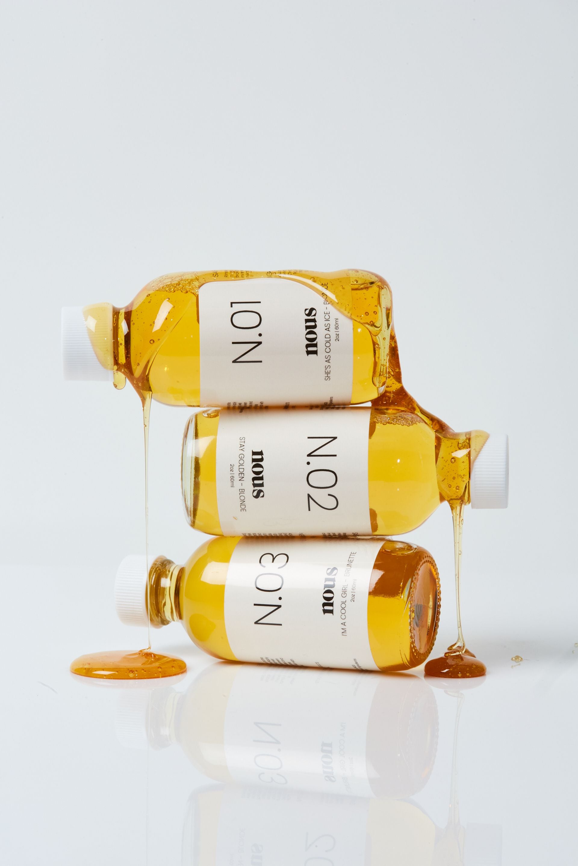 nous hair gloss collection featuring N.01, N.02, and N.03 stacked with golden gloss dripping on white background